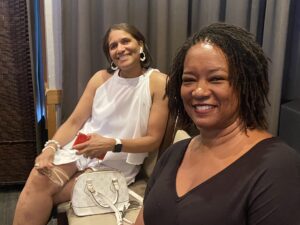 Two women sitting and smiling wearing casual attire